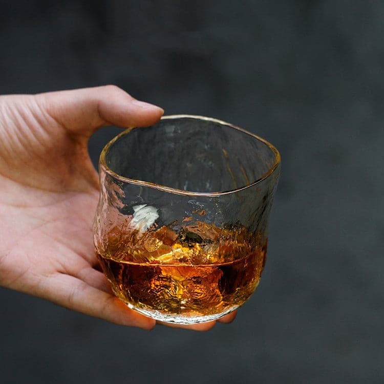 Hand holding a Japanese Style Whiskey Glass with meditation-inspired design, filled with whiskey, highlighting its unique craftsmanship and elegant appearance.